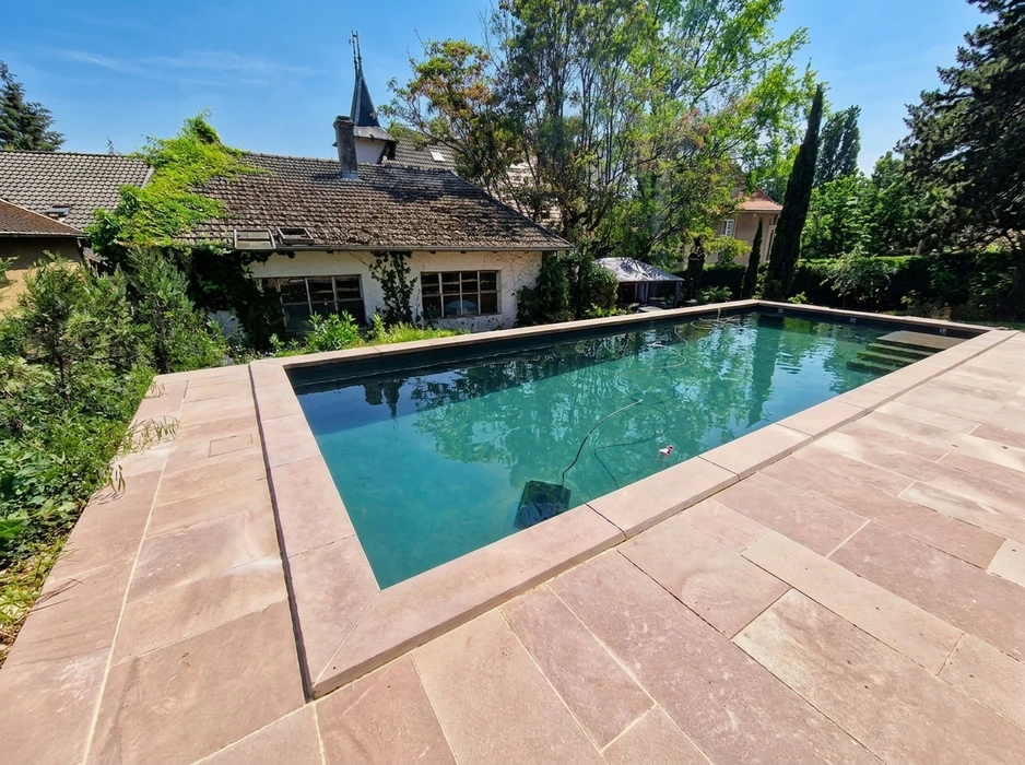 Piscine rectangulaire extérieure à débordement partiel, dallage périmétrique en grès rose brossé grand format