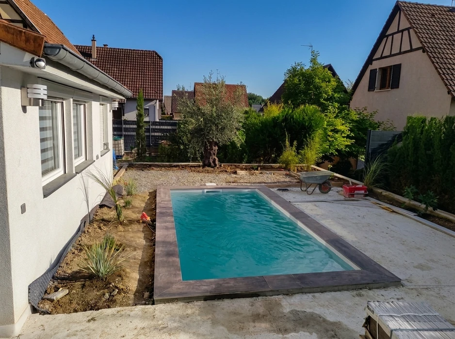 Jardin résidentiel en cours d'aménagement avec piscine rectangulaire enterrée, eau turquoise, margelles en carrelage grès cérame imitation bois
