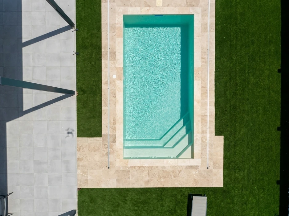 Vue aérienne d'une piscine rectangulaire aux eaux turquoise, entourée d'un dallage en travertin beige