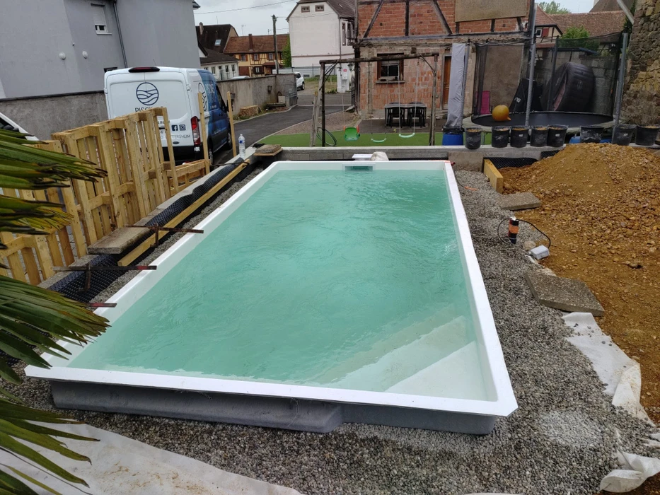 Vue aérienne d'une piscine coque polyester rectangulaire aux angles arrondis, finition blanc nacré, eau turquoise cristalline